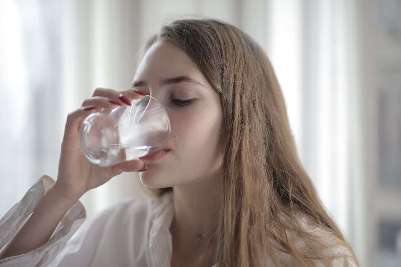 A young woman sipping water from a glass in a bright room.
